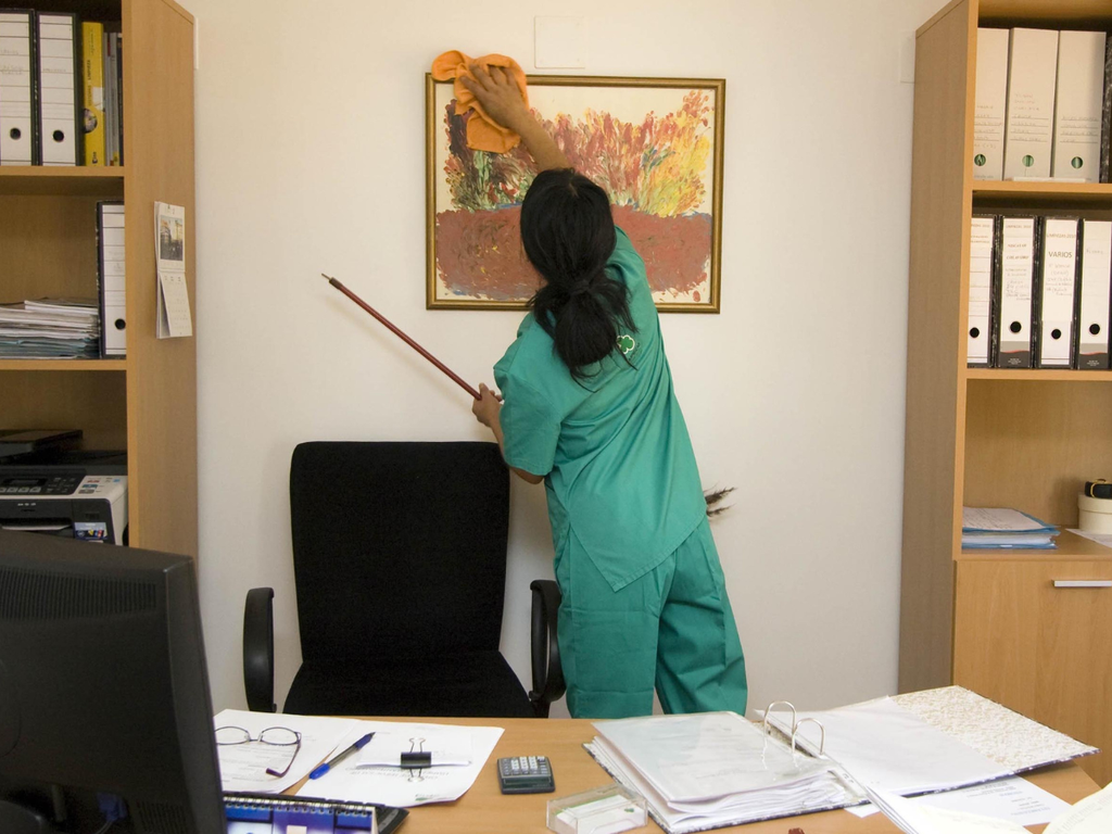 A person in a green uniform cleans a framed painting on an office wall, highlighting why it is important to choose a commercial cleaning company in Marietta.