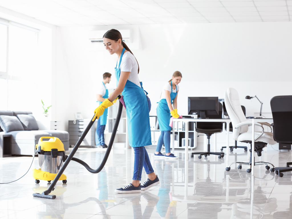 Three professional cleaners wearing blue aprons and yellow gloves provide commercial cleaning services in an office space.