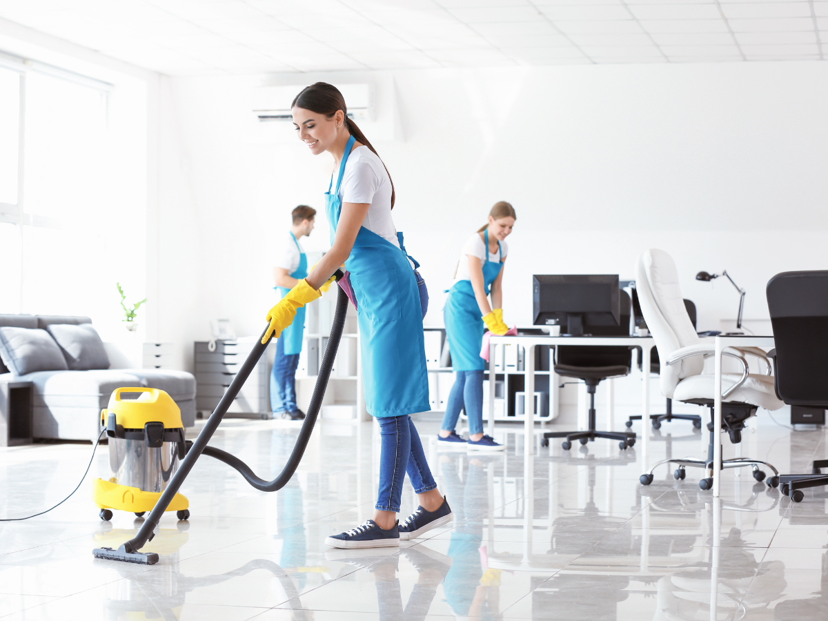 Three cleaners in blue aprons and yellow gloves clean an office, illustrating a guide on how to choose a commercial cleaning company in Marietta.