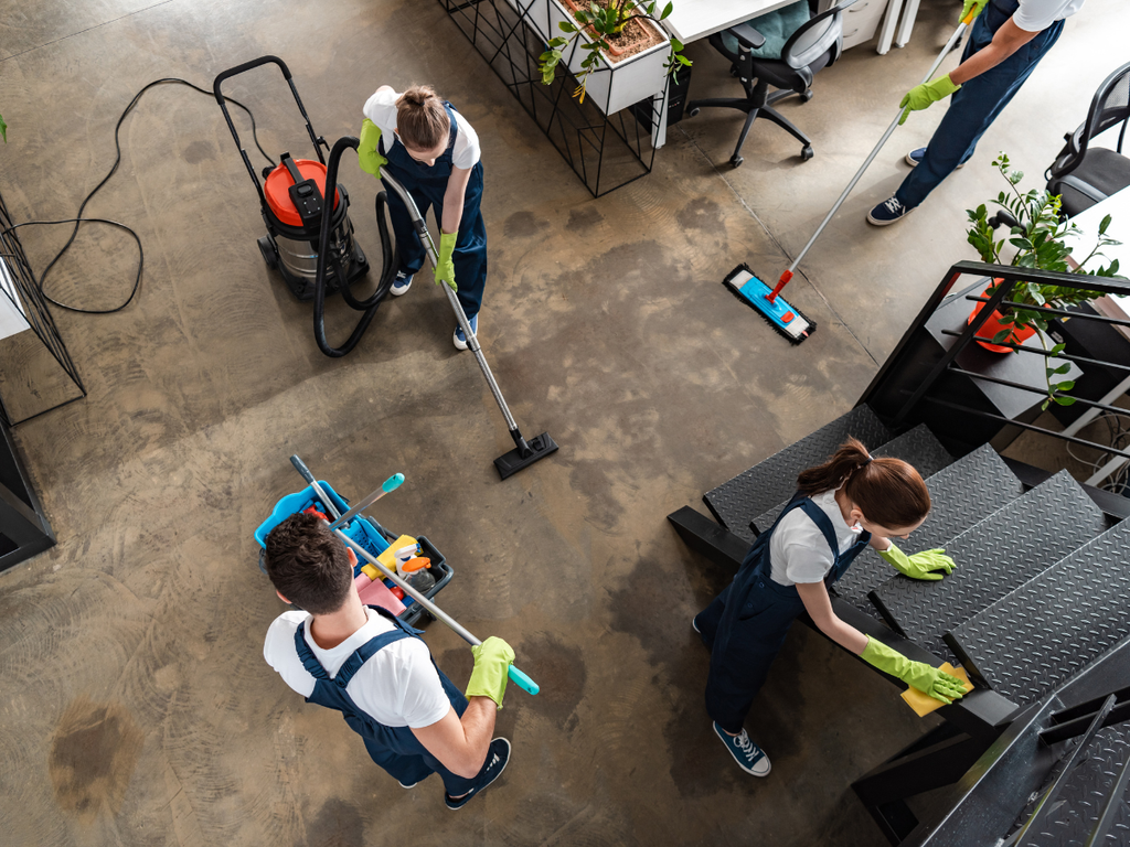 Four professional cleaners in navy uniforms and green gloves cleaning an office space, reflecting the office cleaning cost in Marietta.