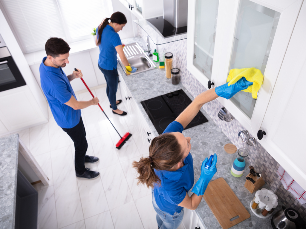 Three professional cleaners in matching blue uniforms performing a house cleaning service in a kitchen.